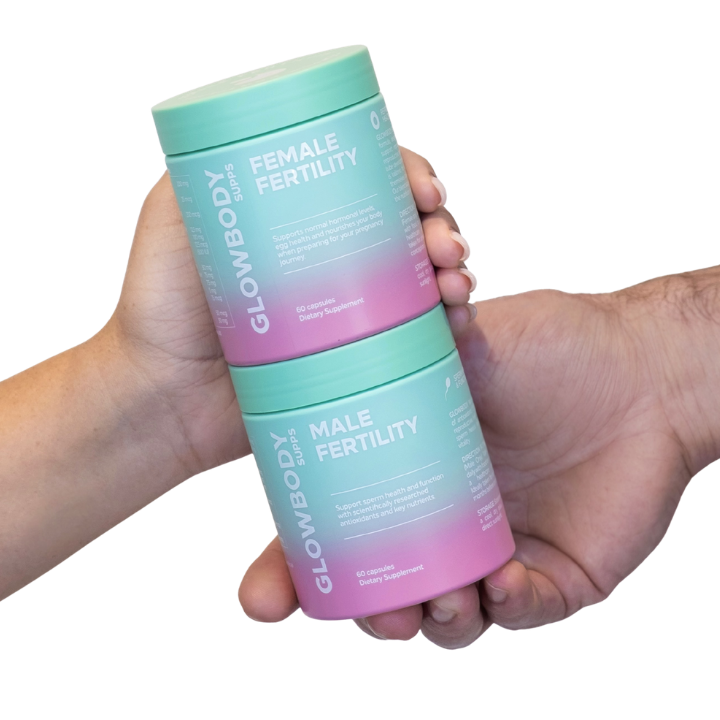 Two Glowbody Supps cylindrical containers labeled 'Female Fertility' and 'Male Fertility' held by a hand against a white background.